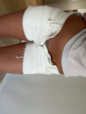 Vita lågmidjade jeansshorts - Säljer ett par vita lågmidjade jeansshorts med råa kanter och dubbla knappar framtill. Endast använd 1 gång tidigare, men köpt förra sommaren från Nelly. Storlek S 