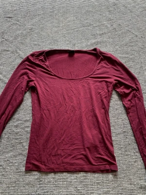 Vinröd långärmad topp med slits - Säljer en vinröd långärmad topp med rund halsringning och liten slits vid ärmslutet. Toppen är i mjuk bomull och har en slim passform som sitter snyggt på kroppen. 