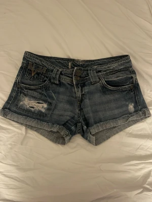 Blå denimshorts med slitningar - Snygga lätt mörkblå denimshorts med slitna detaljer. Klassisk femficksmodell med knapp och dragkedja framtill. Sparsamt använda och supersnygga!