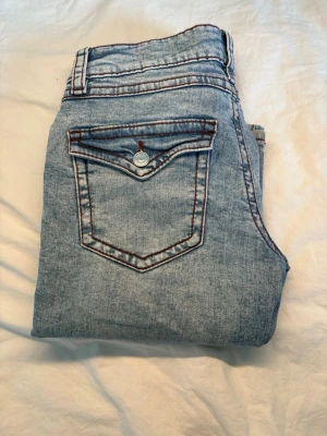 Ljusblå  bootcut jeans - Säljer ett par ljusblå jeans med bootcut-modell och slitningar på benen. Jeansen är i storleken 164.