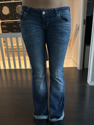 Blå bootcut jeans med uppvik - Säljer ett par blå bootcut jeans med uppvikta benslut. Jeansen har klassisk femficksdesign och är gjorda i denim med en snygg tvätt. Perfekta för dig som gillar en avslappnad men ändå trendig look.