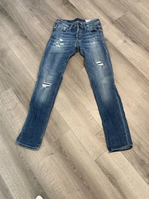 Blå slitna jeans med raka ben - Säljer ett par blå jeans med raka ben och slitningar på både fram- och baksida, storlek 29/32
