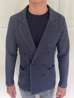 John Henric Kavaj - Mörkblå dubbelknäppt kavaj från John Henric. Tillverkad i ett mjukt, stickat material som ger en avslappnad men stilren look. Modell på bild 182cm 78kg, passar ca 175-188. Skriv vid minsta fundering!