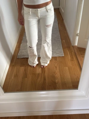 Vita bootcut jeans med slitningar - Säljer ett par vita bootcut jeans med slitningar på låret och knät. Jeansen har fem fickor, normal midja och är tillverkade i ett denimtyg med lite stretch. Perfekta för en trendig och avslappnad look.
