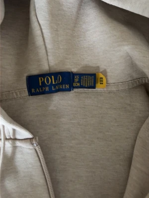 Beige hoodie från Polo Ralph Lauren - Snygg sand beige hoodie från Polo Ralph Lauren med dragkedja framtill och justerbar huva. Klassisk design med diskret logga på bröstet och mjukt material som känns skönt mot huden. Perfekt för en avslappnad och stilren look. Kvitto har jag iaf någon undrar om den är äkta. Org pris 900 kr och använd få gånger 