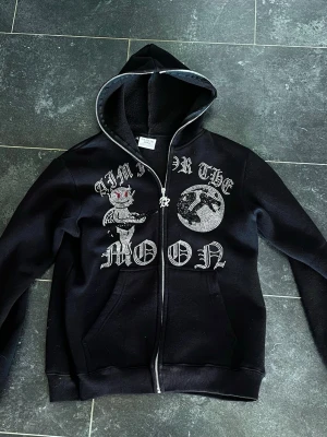 Aim for the moon zip hoodie - Säljer en svart zip hoodie då jag knappt använt den. Det är en unik tröja som är både snygg och bekväm. Det är size medium och modellen är 185cm