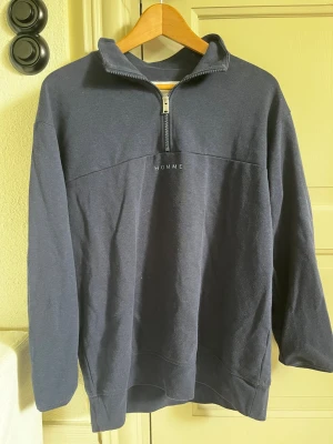 Mörkblå halfzip hoodie med tryck - Mörkblå hoodie med halv dragkedja och hög krage. Trycket 'HOMME' syns framtill på bröstet. Hoodien har en avslappnad passform och är tillverkad i mjukt bomullstyg. Perfekt för en chill och stilren look.