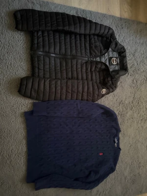 Svart dunjacka från Colmar - Snygg svart dunjacka från Colmar med quiltad design och hög krage. Jackan har två dragkedjeförsedda fickor framtill och hel dragkedja. Perfekt för kalla vinterdagar och riktigt lätt att bära. Klassisk och stilren look som passar till det mesta.