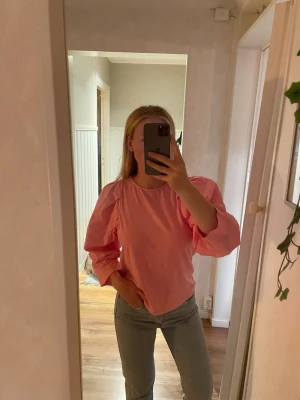 Rosa blus med puffärmar från Lindex - Snygg rosa blus från Lindex med puffiga långärmar och rund halsringning. Blusen har en avslappnad passform och är gjord i ett mjukt, tunt material som känns skönt mot huden. Perfekt för dig som vill ha en trendig och färgglad look.