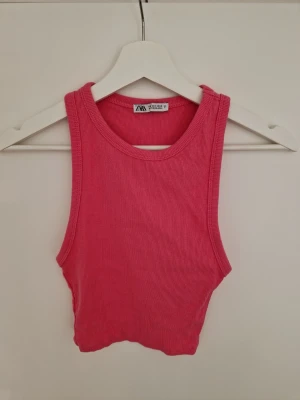 Rosa ribbad linnetopp från Zara - Säljer en rosa ribbad linnetopp från Zara i storlek S. Toppen är croppad och ärmlös med rund halsringning och stretchigt material som sitter snyggt på kroppen. Perfekt till sommaren och enkel att matcha med jeans eller kjol.