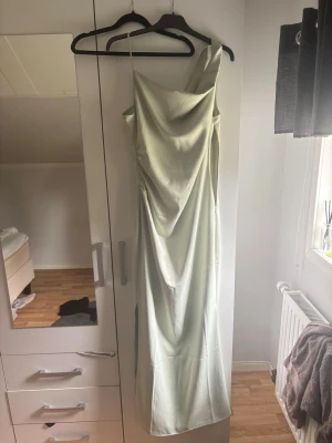 Ljusgrön långklänning med slits - Säljer en elegant ljusgrön långklänning med smala axelband och draperad urringning. Klänningen har en smickrande passform och en liten slits på sidan för extra rörelsefrihet. Perfekt för student eller bal!