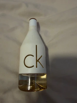 CK parfymflaska i vit och glas - Säljer en stilren parfymflaska från CK med vit matt överdel och genomskinlig glasbotten. Flaskan har en unik design med stora bokstäver 'ck' utskurna i det vita materialet. Perfekt för dig som gillar minimalistisk och modern stil.