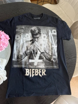 Justin Bieber t-shirt merch - Cool svart t-shirt med stort tryck av Justin Bieber på framsidan och texten 'Bieber' under motivet. Klassisk passform och rund hals. Perfekt för dig som gillar musik och vill sticka ut med en unik bandtröja. Är aldrig använd, bara legat i min garderob. Är i storlek S men passar XS.  Äkta merch från Purpose-tour. 