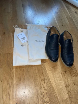 Loro Piana Open walks - Säljer ett par stilrena marinblå loafers från Loro Piana i mjukt, strukturerat läder. Medföljer två  dustbags med logga. Perfekta för dig som gillar tidlös design. Köpta från vestiare collective med äkthetskontroll. 