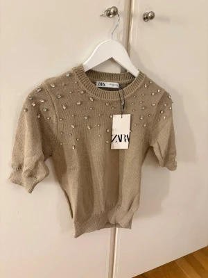 Stickaftopp zara  - Stickad topp med rund halsringning, korta ärmar och strassdetaljer. Aldrig använd och prislappen sitter kvar!