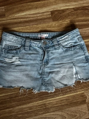 Ljus jeanskjol med lågmidja från Gina Tricot  - Kort ljusblå jeanskjol med slitna detaljer och rå kant. Kjolen har broderade bakfickor, bälteshällor och knappstängning framtill. Perfekt för en avslappnad och trendig look. Säljer på grund av att dom tyvärr är trasiga (de sista bilden) men dom går att laga genom att sy men tyvärr har jag inte material osv. Orginal pris 299kr