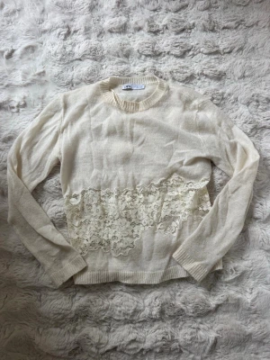 Vit stickad tröja med spetsdetalj - Snygg vit stickad tröja från Zara med lång ärm och rund halsringning. Tröjan har en bred spetsdetalj i midjan som ger en romantisk touch. Materialet är mjukt och lätt, perfekt för lager på lager. Passar till både jeans och kjol. Liten liten fläck på bild 2, syns ej