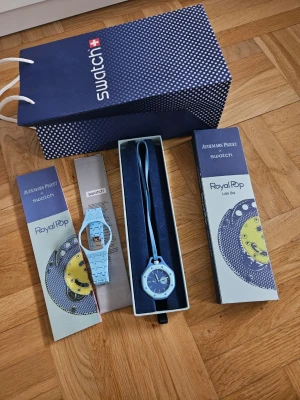 Audemars Piguet x Swatch Lan Ba Royal Pop - Säljer en Swatch Royal Pop klocka i samarbete med Audemars Piguet. Klockan är ljusblå med matchande armband och urtavla. Kommer i originalförpackning med snygg design och Swatch-påse. Perfekt accessoar för dig som gillar färg och modern stil.
