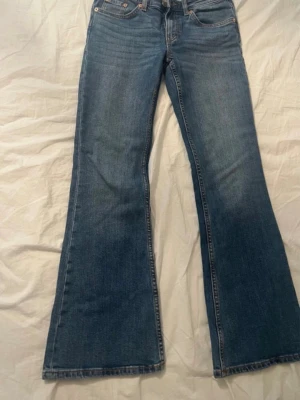 Blå bootcut jeans - Säljer ett par klassiska blå bootcut jeans i storlek XS med kort längd. Jeansen har fem fickor, normalhög midja och snygga kontrastsömmar.
