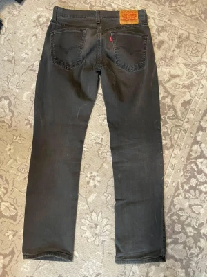 Levis 514 - Säljer ett par gråa vintage jeans från Levi's med klassisk femficksmodell och raka ben. Jeansen har en diskret röd Levi's-tag på bakfickan och läderpatch i midjan. Materialet är denim med en mjuk känsla och passformen är normal. (Litet hål vid bungen men kan sys enkelt)