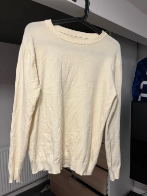 Krämvit stickad tröja - En enkel och stilren krämvit stickad/kamsir tröja med rund halsringning och långa ärmar. Tröjan har ribbade muddar vid ärmslut och nederkant. Perfekt att matcha med jeans eller kjol för en clean look.