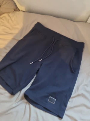 Mörkblå shorts från Dolce & Gabbana - Snygga mörkblå shorts från Dolce & Gabbana med snörning i midjan och en metallbricka med logga framtill. Shortsen har en avslappnad passform och är perfekta för sommardagar. Tillverkade i mjukt bomullsmaterial för maximal komfort.