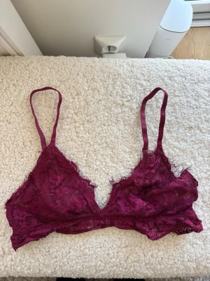 Vinröd spetsbralette med tunna band - Säljer en vinröd bralette i spets med tunna axelband och triangelformade kupor. Bh:n har dekorativa spetsdetaljer och en mjuk, osydd kant nedtill. Perfekt för dig som gillar en lätt och bekväm stil med romantisk känsla.