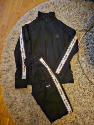 Svart tracksuit från BOSS med revärer - Helt nytt Set med byxor och zip tröja från Boss. Strl. Medium 