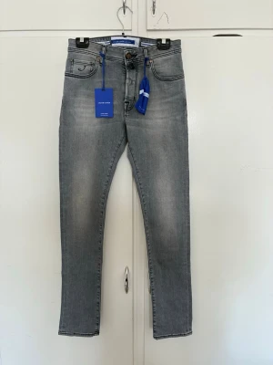 Grå jeans från Jacob Cohen - Snygga grå jeans från Jacob Cohen med klassisk femficksmodell och diskret tvättade detaljer. Jeansen har normalhög midja, smal passform och är tillverkade i stretchigt denim för extra komfort. Perfekta för en trendig och avslappnad look.