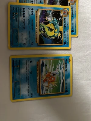 Pokémonkort - Säljer ett gäng Pokémonkort inklusive Magikarp och Gyarados samt ett vitt plastalbum med genomskinliga plastfickor för förvaring av samlarkort. Perfekt för dig som vill organisera och skydda dina kort. Albumet är smidigt och lätt att ta med.