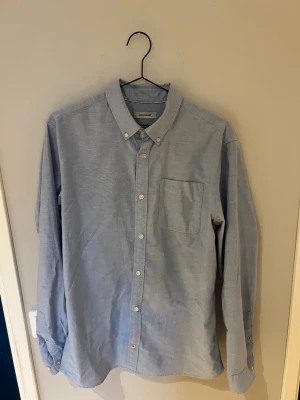 Ljusblå skjorta från Jack & Jones - Säljer en stilren ljusblå skjorta från Jack & Jones i bomull. Skjortan har klassisk krage med knappar, bröstficka och långa ärmar. Perfekt för dig som gillar enkel och clean stil.
