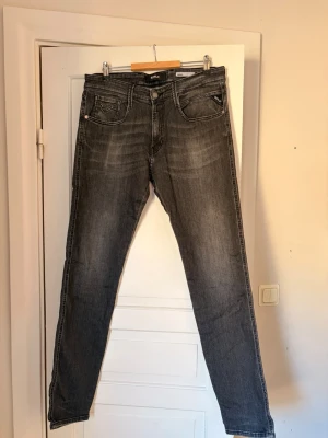 Gråa raka jeans med slitningar - gråa replay jeans med raka ben. Storlek - W33 L34 Jeansen har fem fickor, normal midja och klassisk knappgylf. Materialet är denim med en tvättad look. Modellen är anbass. 