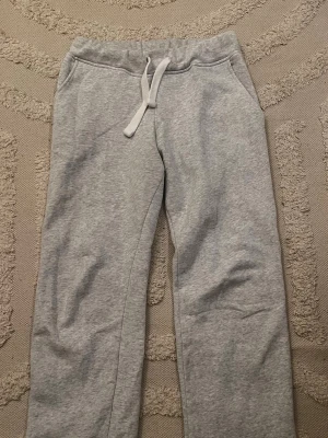 Grå russe mjukisbyxor  - Säljer ett par klassiska grå mjukisbyxor från russemerch  med resår i midjan och vit dragsko. Byxorna har raka ben och två fickor fram. Perfekta för chill dagar hemma eller när du vill vara extra bekväm. Tillverkade i mjukt sweatshirtmaterial.
