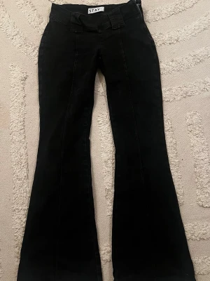 Svarta utsvängda jeans från STAY - Säljer ett par svarta jeans från STAY med utsvängda ben och låg midja. Jeansen har breda hällor och en clean look utan synliga detaljer framtill. 