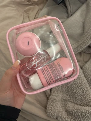 Sol de Janeiro rosa necessär med produkter - Säljer en genomskinlig necessär med rosa kant från Sol de Janeiro. Innehåller tre produkter: en body wash, en spray och en kräm, alla i rosa och vitt. Perfekt för resan eller gymväskan. Smidig storlek och snygg design.