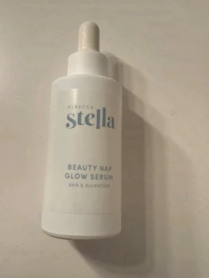 Rebecca Stella Beauty Nap Glow Serum - Glow serum från Rebecca Stella med AHA och allantoin. Kommer i en vit flaska med pipett och stilren design. Perfekt för dig som vill boosta glowet i din hudvårdsrutin.