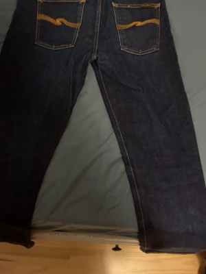 Mörkblå raka jeans - Säljer ett par mörkblå jeans med raka ben och klassiska kontrastsömmar. Jeansen har en enkel design utan synligt märke och passar perfekt till en avslappnad stil. Materialet ser ut att vara klassisk denim med en stadig känsla.