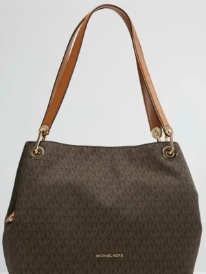 Michael Kors brun väska - Snygg brun handväska från Michael Kors med klassiskt MK-mönster över hela väskan. Väskan har två breda axelband i brunt läder och guldfärgade metalldetaljer. Perfekt storlek för att få plats med allt du behöver. Stängs med dragkedja.