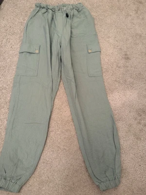 Ljusgröna cargobyxor Gaudi Jeans - Snygga ljusgröna cargobyxor från Gaudi Jeans med resår i midjan och benslut. Byxorna har stora sidofickor med lock och knapp, samt dragsko i midjan för skön passform. Perfekta för en avslappnad och trendig stil.