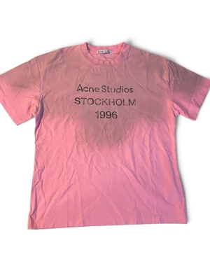 Rosa Acne Studios t-shirt | S/M - Säljer en rosa t-shirt från Acne Studios med trycket 'Acne Studios STOCKHOLM 1996' på bröstet. Klassisk rund hals och korta ärmar. Perfekt för dig som gillar streetwear och vill ha något från ett ikoniskt svenskt märke.