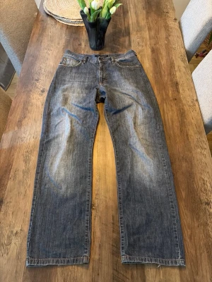 Gråa bootcut jenss - Säljer ett par gråblå jeans med bootcut och klassisk femficksdesign. Jeansen har en något tvättad look och är tillverkade i denim. Perfekt för dig som gillar en enkel och tidlös stil.