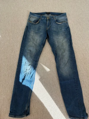 Blå jeans från Martinique  - Säljer ett par blå jeans från Martinique med klassisk femficksdesign och snygga slitningar på låren. Jeansen har raka ben och är gjorda i denim med ljusare tvätt på framsidan. Perfekta för dig som gillar en avslappnad och trendig look.