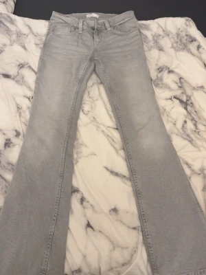 Ljusgrå bootcut jeans - Säljer ett par ljusgrå bootcut jeans med snygga sömdetaljer på bakfickorna. Jeansen har klassisk femficksmodell och är tillverkade i mjukt denimtyg. Perfekta för dig som gillar en retroinspirerad look med utsvängda ben.