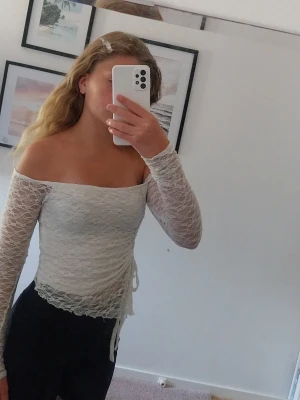 Vit offshoulder spets topp - Säljer en vit offshoulder topp i spets med lång ärm och snörning i sidan. Toppen är croppad och har en feminin, romantisk vibe med transparent spetsmaterial. Perfekt för dig som vill ha en trendig och snygg topp till sommaren💞💕💞💕
