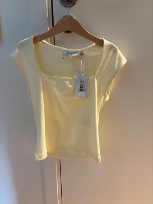 Ljusgul croppad topp från RYVLS - Trendig ljusgul croppad topp från RYVLS Stockholm med fyrkantig ringning och ärmlös design. Perfekt för dig som vill ha en enkel men snygg topp till sommaren. Tillverkad i mjuk bomull för skön känsla.