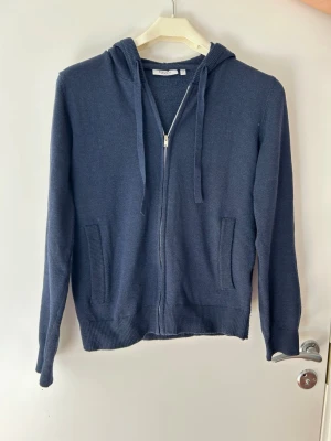 Mörkblå zip hoodie med huva - En stilren mörkblå hoodie med dragkedja framtill och två fickor. Tröjan har ribbade muddar vid ärmslut och nederkant samt en klassisk huva med dragsko. Perfekt för en avslappnad look och enkel att matcha med det mesta. Hör av dig om du har några frågor!