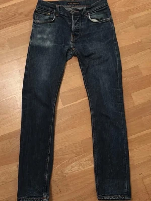 Nudie jeans grim tim w29 l30 - Snygga mörkblå jeans från Nudie med smal passform och klassiska fem fickor. Jeansen har slitningar framtill och Nudies ikoniska broderi på bakfickorna. Tillverkade i denim med en cool tvätt och orangea sömmar.