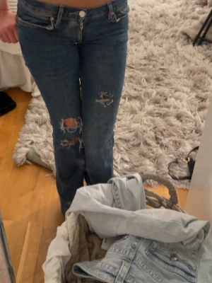 mörkblå lågmidjade slitna jeans med hål - mörkblå jeans som jag sytt om till lågmidjat, slitningen är egengjord!! över ena slitningen är det ett kryss gjort med penna, ingen aning ifall det går bort i tvätten men det syns inte så mycket. även lite slitage längst ned (andra bilden)
