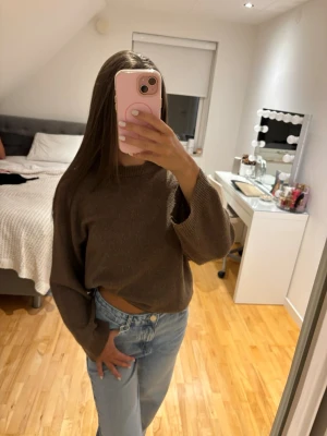 Brun oversized stickad tröja - Mysig brun stickad tröja med avslappnad passform och långa ärmar. Tröjan har en enkel design med rund halsringning och ribbade muddar. Perfekt för lager på lager och passar till både jeans och kjol.
