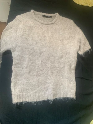 Ljusgrå fluffig stickad tröja XS - Mysig ljusgrå stickad tröja från 157 i storlek XS. Tröjan har korta ärmar, rund halsringning och är gjord i ett fluffigt, mjukt material som känns skönt mot huden. Perfekt för lager på lager och en chill look.